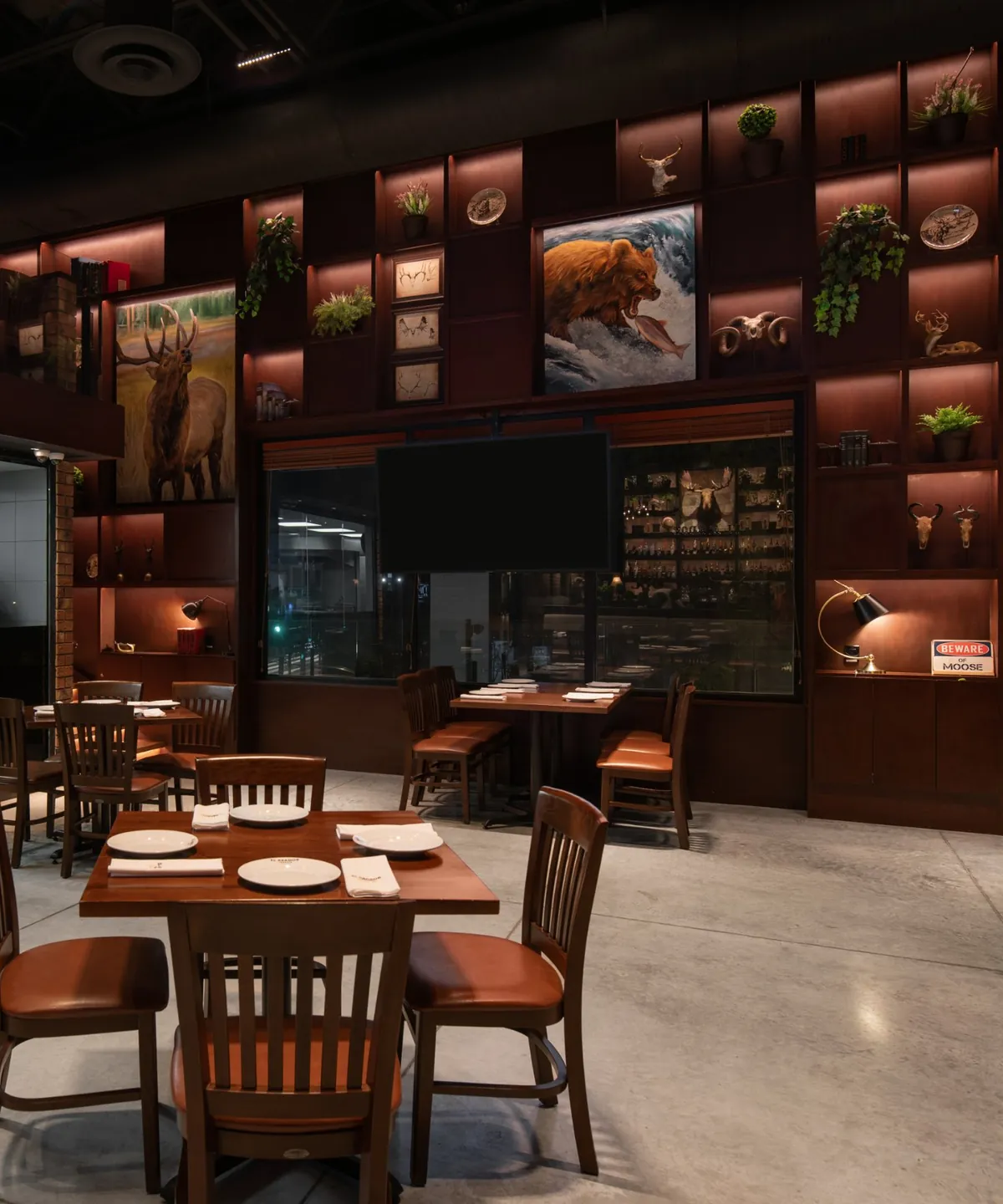 Fotografía del proyecto El Asador Terraza del portafolio LUCONSA: salón con mesas de madera y estantería iluminada en un muro de doble altura