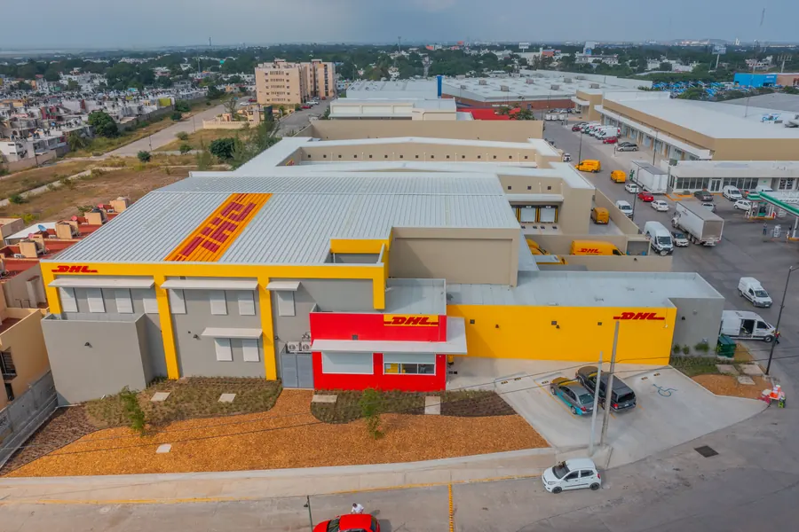 Fotografía del proyecto DHL del portafolio LUCONSA: fachada amarilla, roja y gris del edificio con jardín frontal