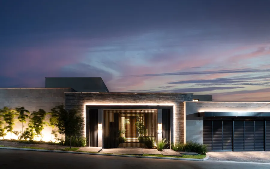 Fotografía del proyecto Residencias del portafolio LUCONSA: fachada de piedra con acceso enmarcado por luz y celosía metálica al atardecer